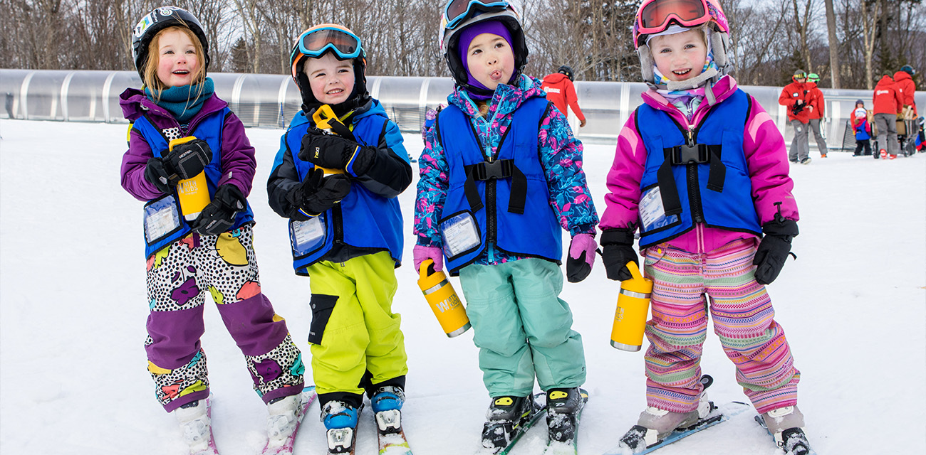 Group of children in colorful ski outfits smiling on a snowy slope.